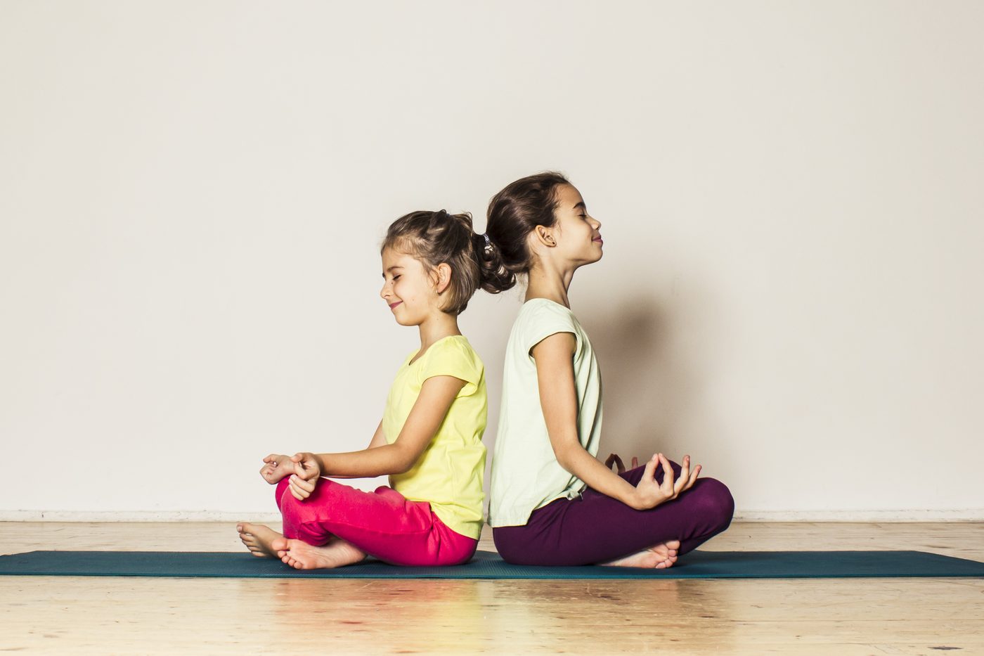 Zwei Kinder sitzen Rücken an Rücken auf der Yogamatte